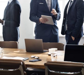 businessmen and businesswoman talking amongst eachother around boardroom table